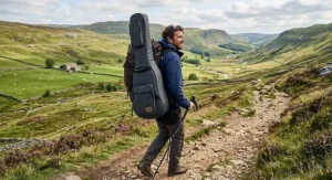 Backpacker carrying a travel guitar in a padded gig bag during a countryside walk