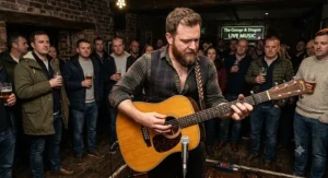 A British acoustic guitarist strumming a dreadnought guitar live on stage during an acoustic gig.