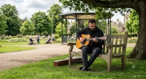 Musician playing an unplugged acoustic guitar outdoors in a British park setting